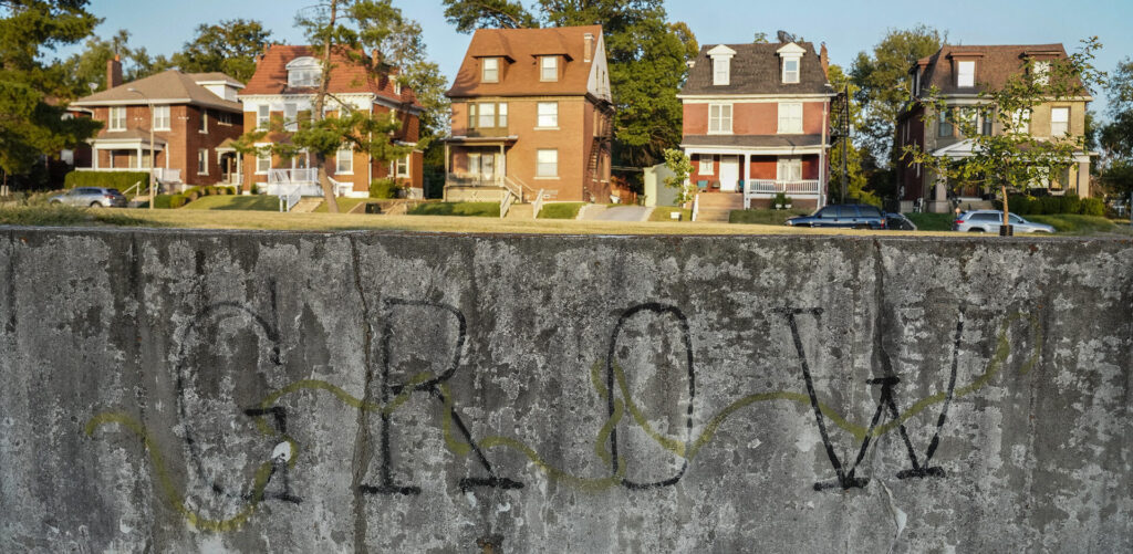 Five multistory brick homes as seen above a concrete wall with the word GROW written on it.