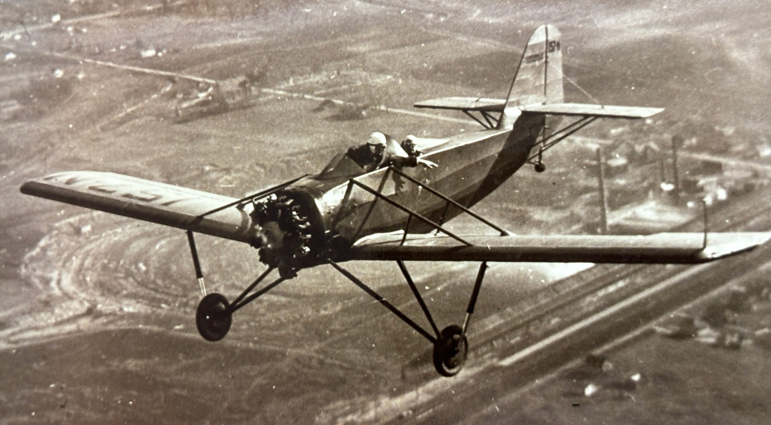 Two people flying in an early airplane.