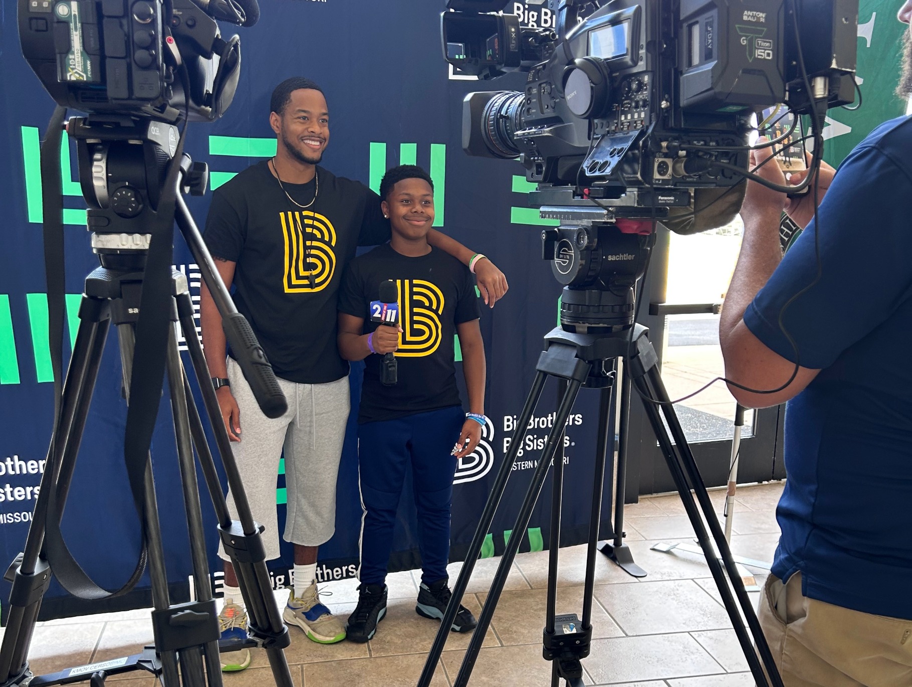 Big Brothers Big Sisters mentor and mentee posing in front of cameras at an event.